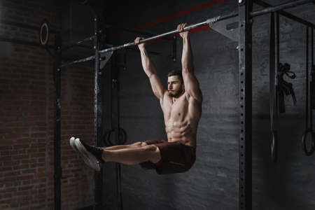 Crossfit athlete doing abs exercise on horizontal bar at the gym. Handsome man doing functional training workout. Practicing calisthenics.の写真素材
