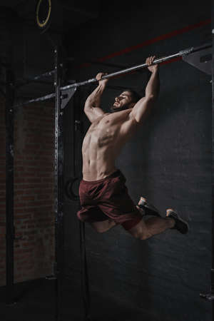 Young crossfit athlete doing pull-ups at the gym. Handsome man doing functional training. Practicing calisthenics.の写真素材