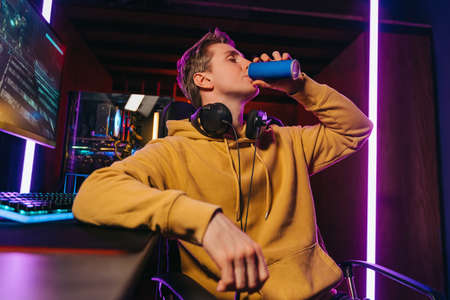 Yong caucasian pro gamer drinking energy drink while playing computer video games