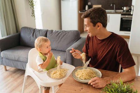 Upper view of dad and baby in high chair eating spaghetti for lunch at kitchen tableの写真素材