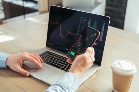 Closeup no face of laptop and phone screen with stock diagrams in hands of crypto trader investorの写真素材