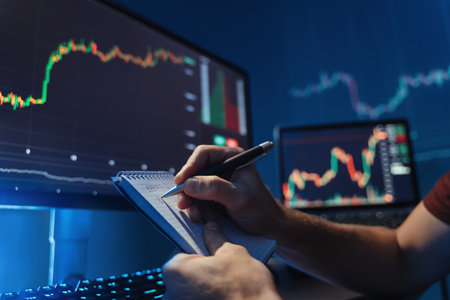 Male hands writing in notepad analyzing diagram of cryptocurrency market at his pc at home