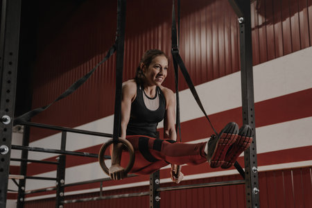 Cheerful crossfit woman doing abs exercises on gymnastic rings