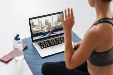 Close up of young fit woman coach in sportswear conducting online fitness training or virtual yoga class on a video conference with laptop. Home workout training. Health practice and wellness conceptの写真素材