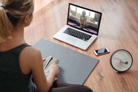 Yoga teacher conducting virtual class at home on a video conference. Young beautiful woman doing an online yoga class in her living room with laptop. Home fitness and workout conceptの写真素材