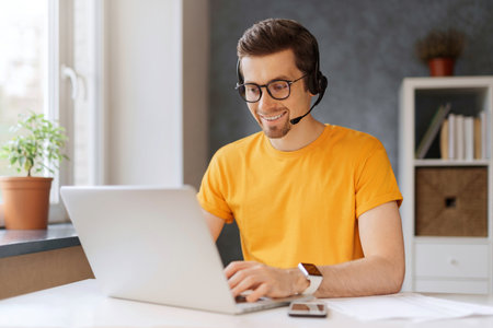 Happy programmer video call with clients and partners. A data center operator works from home. A man wearing glasses and headphones enjoys watching an educational online webinar on his laptopの写真素材