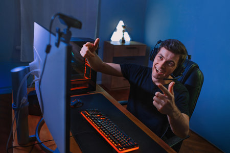 Young handsome vlogger having live stream while playing in online video game at home on PC. Cyber...