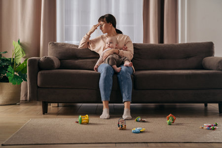 Tired single mother suffering from postpartum depression. Exhausted frustrated woman holding her toddler baby on knees, feeling stressed with sleepless nights and stressful motherhood difficultiesの写真素材
