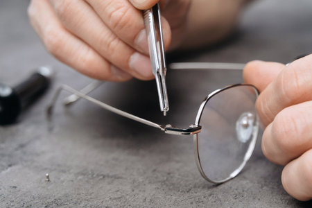Closeup of opticians hands repairing glasses with special tools and equipment in clinic office or optics. New eyeglasses production for optometrist eyewearshopの写真素材
