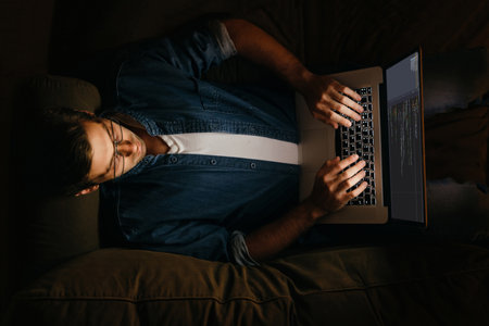 Top view of male programmer laying on sofa and working at his laptop. Overworked coder working from home at night.の写真素材