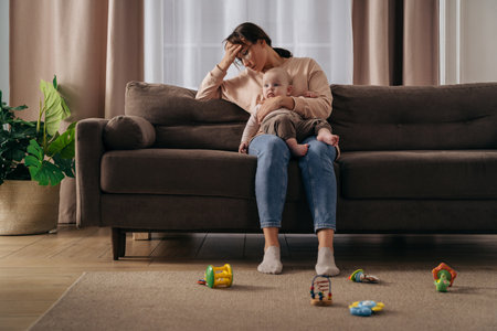 Postnatal depression and stressful motherhood concept. Exhausted woman feeling headache, holding her little baby, suffering from sleepless nights and problems. Single mom take care of her baby aloneの写真素材