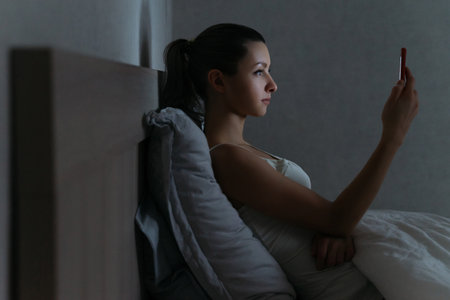 Young woman using her smartphone addictively late at night in her bed. Gadget dependence concept.の写真素材