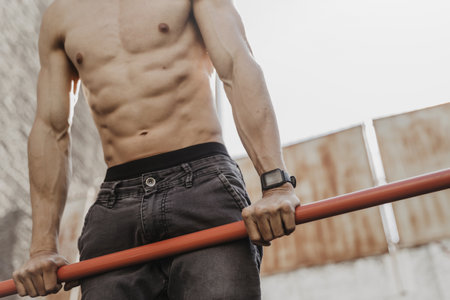 Close up of shirtless athlete practicing calisthenics with smartwatch on his wrist. Young man doing...