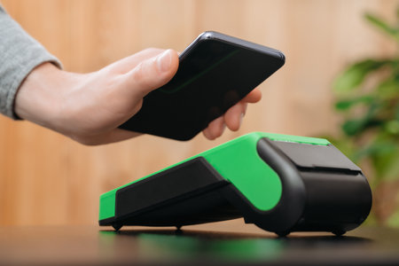 Closeup of mans hand holding smartphone near nfc payment terminal. Customer using phone for...