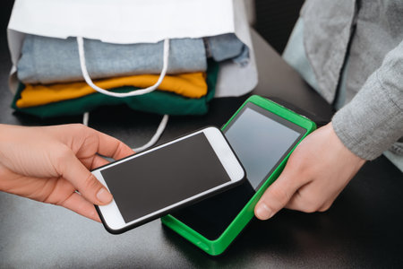 Closeup of woman using smartphone for contactless payment for purchase in clothing store. Mobile,...