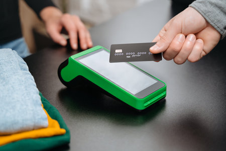 Closeup view, male customer using bank credit card for contactless payment by nfc terminal on counter while doing shopping in clothing store. Contactless and NFC technology conceptの写真素材