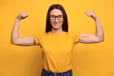 Strong powerful woman with dark hair, eyeglasses and toothy smile raises arms and shows biceps,...