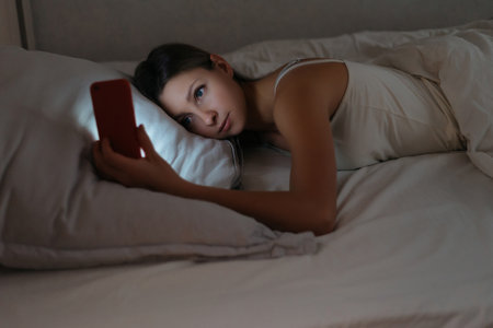 Young woman watching her smartphone instead sleeping at night. Gadget dependence and overuse concept. Social network and phone addictionの写真素材