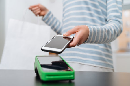 Female customer paying for purchase through smartphone using NFC technology. Closeup of womans hand...