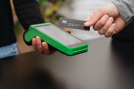 Closeup of male right hand holding bank credit card on a NFC payment terminal held by a womans hand...