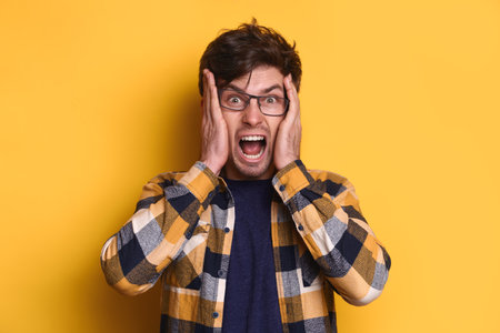 Portrait of frustrated exhausted evil guy tired of lots of hard or routine work, lose temper, screaming, hold his hands on head, isolated over yellow background. Desperate mad man looking crazyの写真素材