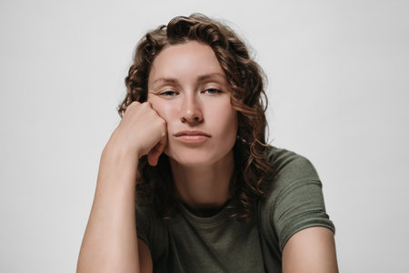 Displeased tired sleepy curly woman, propping his cheek, looking bored, isolated against white backgroundの写真素材