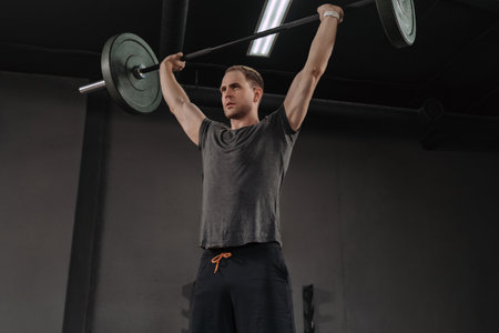 Strong muscular man holding heavy barbell overhead at crossfit gym, doing military press exercises as a part of functional training. Weightlifter exercising with barbell.の写真素材