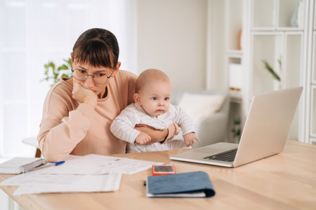 Young upset mother frustrated with financial problems, trying to find a solution while babysitting with her little child. Single unhappy mom looking at documents, tired of motherhood difficultiesの写真素材