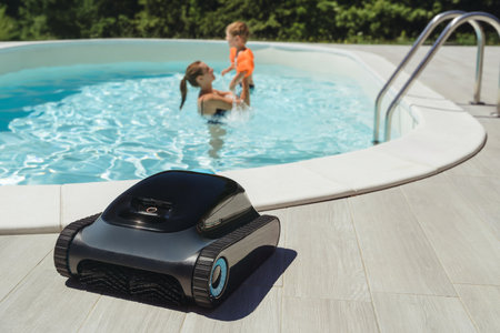 A robotic pool cleaner on the poolside with a mother and child enjoy swimming in clear blue water on background . Modern pool maintenance cleaning convenience.の写真素材