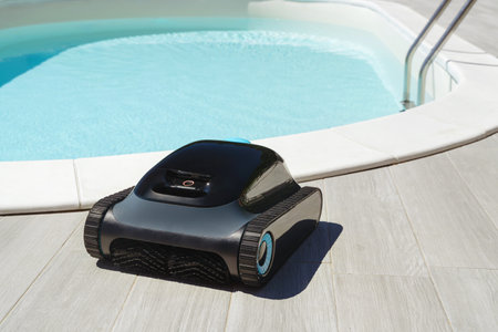 A robotic pool cleaner in front of swimming pool with clear blue water. Modern pool maintenance cleaning convenience. Copy spaceの写真素材