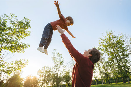 Joyful father playing with his smiling young son, tossing up and catching him in a park at sunset. Family bonding, happy childhood and Fathers day concept. Copy spaceの写真素材