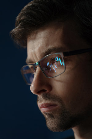 Close up of businessman analyzing trading data late at night, staring at a monitor with stock indexes and economic charts reflecting in his glasses, evaluating investment strategies on crypto market.の写真素材