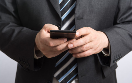 Hands of businessman in black suit who is using a smartphone. Focus on smartphoneの写真素材