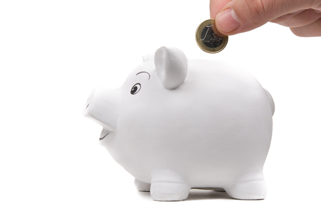 Insert coin in a happy piggy bank. Isolated on white, focus on coin.の写真素材