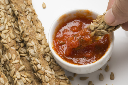 Dipping a breadstick with sunflower seeds in sauceの写真素材
