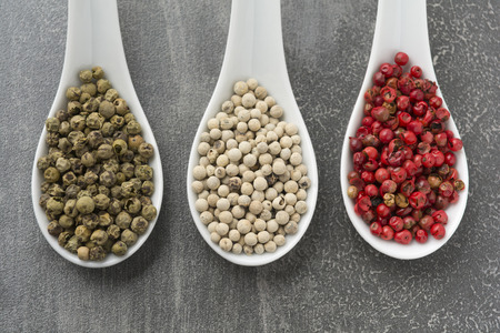 Three white ceramic spoons filled with various peppers on rustic grey backgroundの写真素材
