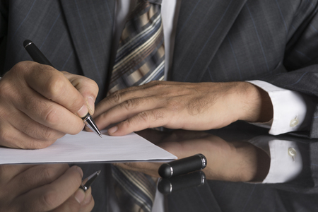 Man in gray suit holds a metal pen and is ready to write on a sheet of paperの写真素材