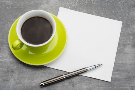 Green cup of coffee with  clean napkin and a metal ballpoint pen on grey backgroundの写真素材