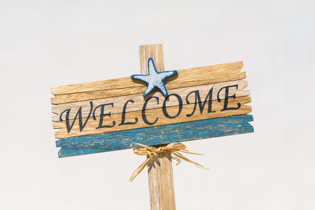 Wooden welcome signpost against white wall, on a summer beach holidays conceptの写真素材