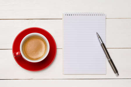 Blank spiral notepad with red cup of coffee over white wooden backgroundの写真素材