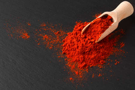 Wooden scoop with ground paprika on black textured background, close upの写真素材