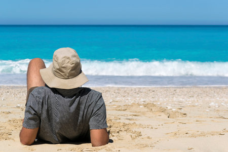 Back view of a man leaning back on his elbows on the beach and looking at the seaの写真素材