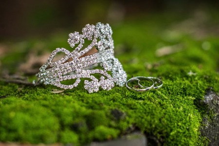 Wedding rings and a sparkling bulky bracelet lie on a rock in the mossの写真素材