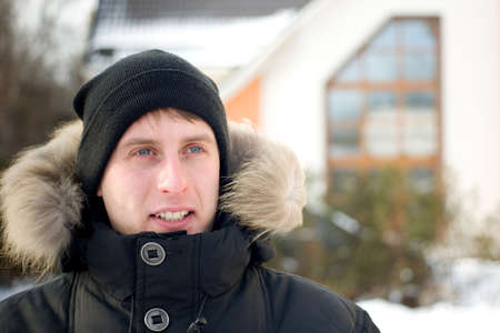 Winter - happy man in cap and warm jacket with furry hood in the yardの写真素材