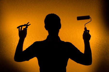 Time for repair and Renovation. Back lit silhouette of man and paint-rollerの写真素材
