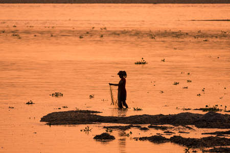 Asian Woman fishing in the river. silhouette at sunset. Village life in Asiaの写真素材