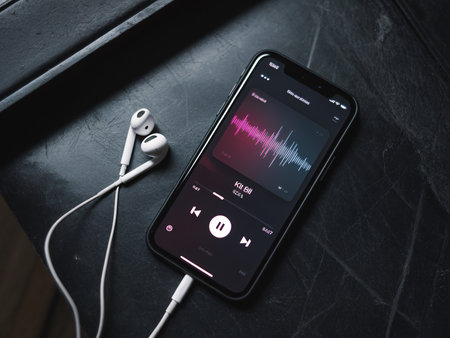 A smartphone displaying a music app with earphones on a dark surface, creating a subtle and modern ambiance.の素材