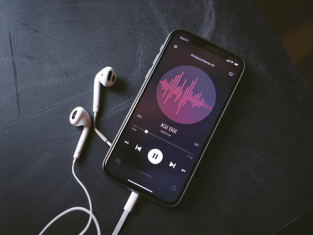 Close-up of a smartphone displaying a music app with earbuds beside it, creating a cozy vibe.の素材