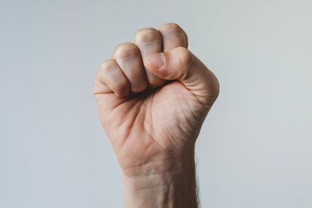 A close-up of a raised fist against a soft grey background, symbolizing strength and determination.の素材