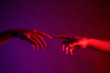Two hands reaching toward each other with vibrant red and purple lighting creating a dramatic contrast.の素材